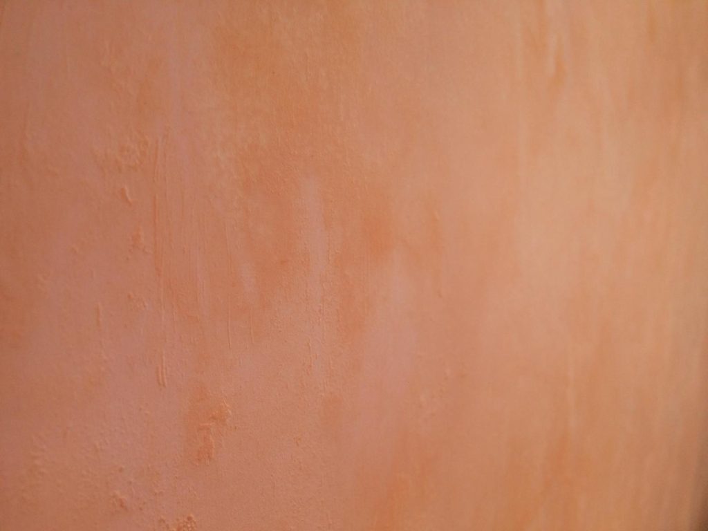 Gros plan d’un mur en enduit ciré couleur terracotta, avant rénovatio