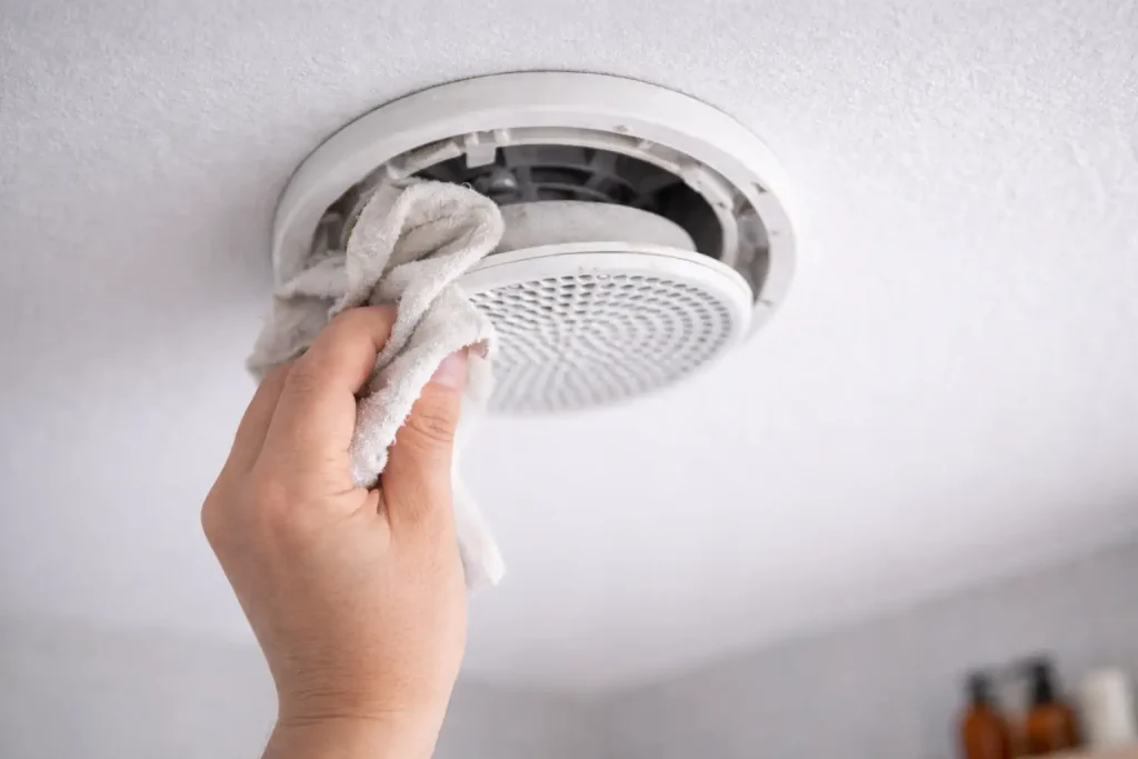 Main nettoyant une bouche d’extraction VMC au plafond avec un chiffon.