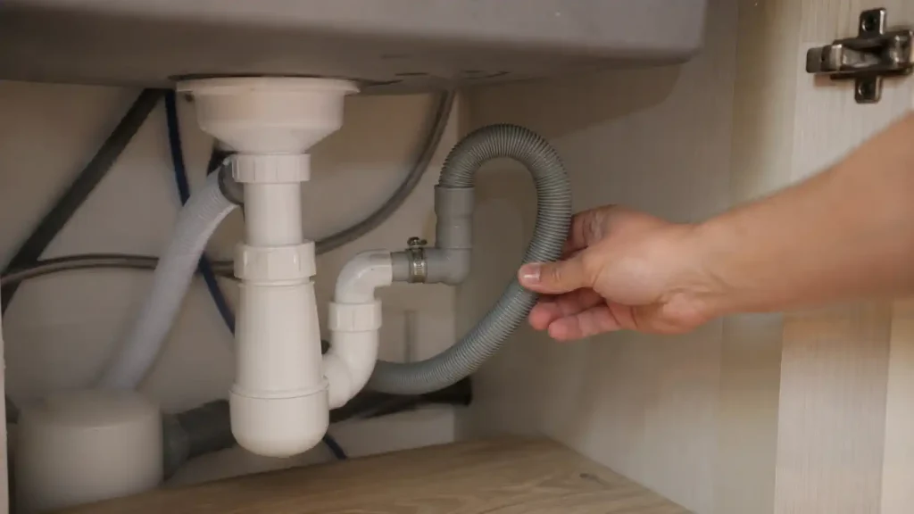 Main vérifiant le tuyau de vidange d’un lave-vaisselle raccordé sous un évier